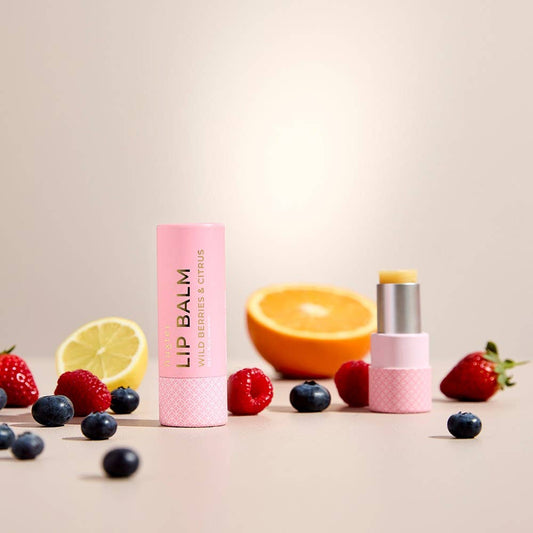 Two lip balms with pink packaging and fruit on a beige background