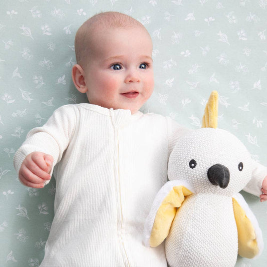 Baby holding a white plush toy with yellow accents against a light blue floral-patterned wall.