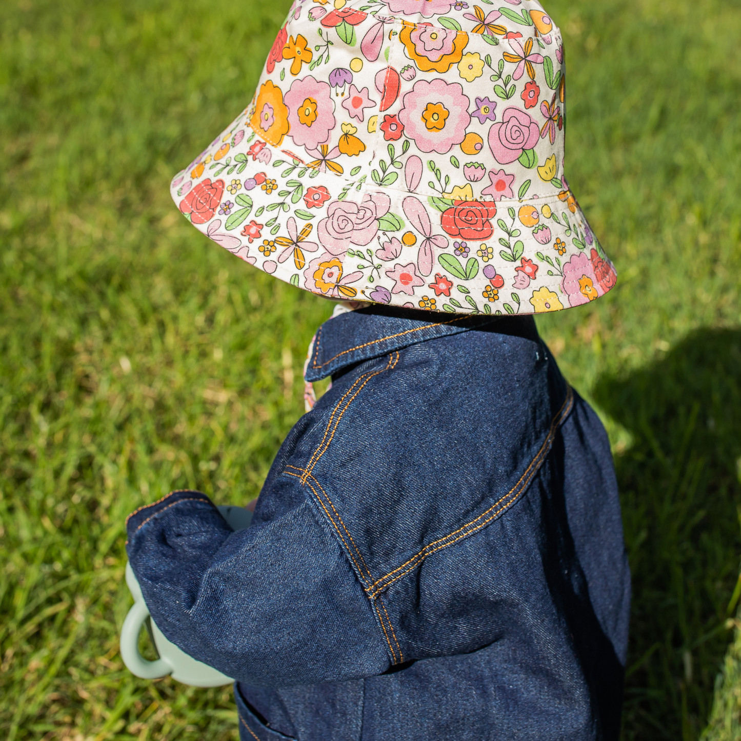 Person wearing a floral-patterned bucket hat and denim jacket on grass