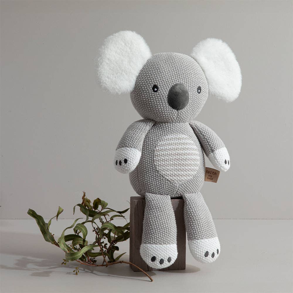 Knitted koala toy on a wooden block with a plain background