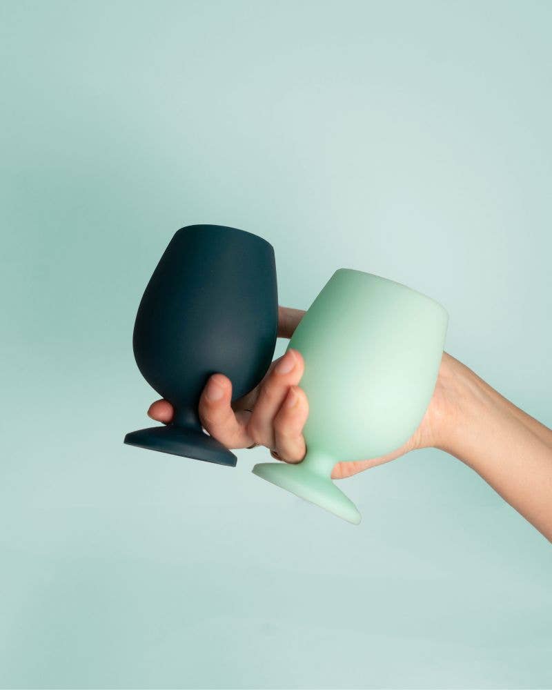 Hand holding two small ceramic cups, one black and one green, against a light blue background.
