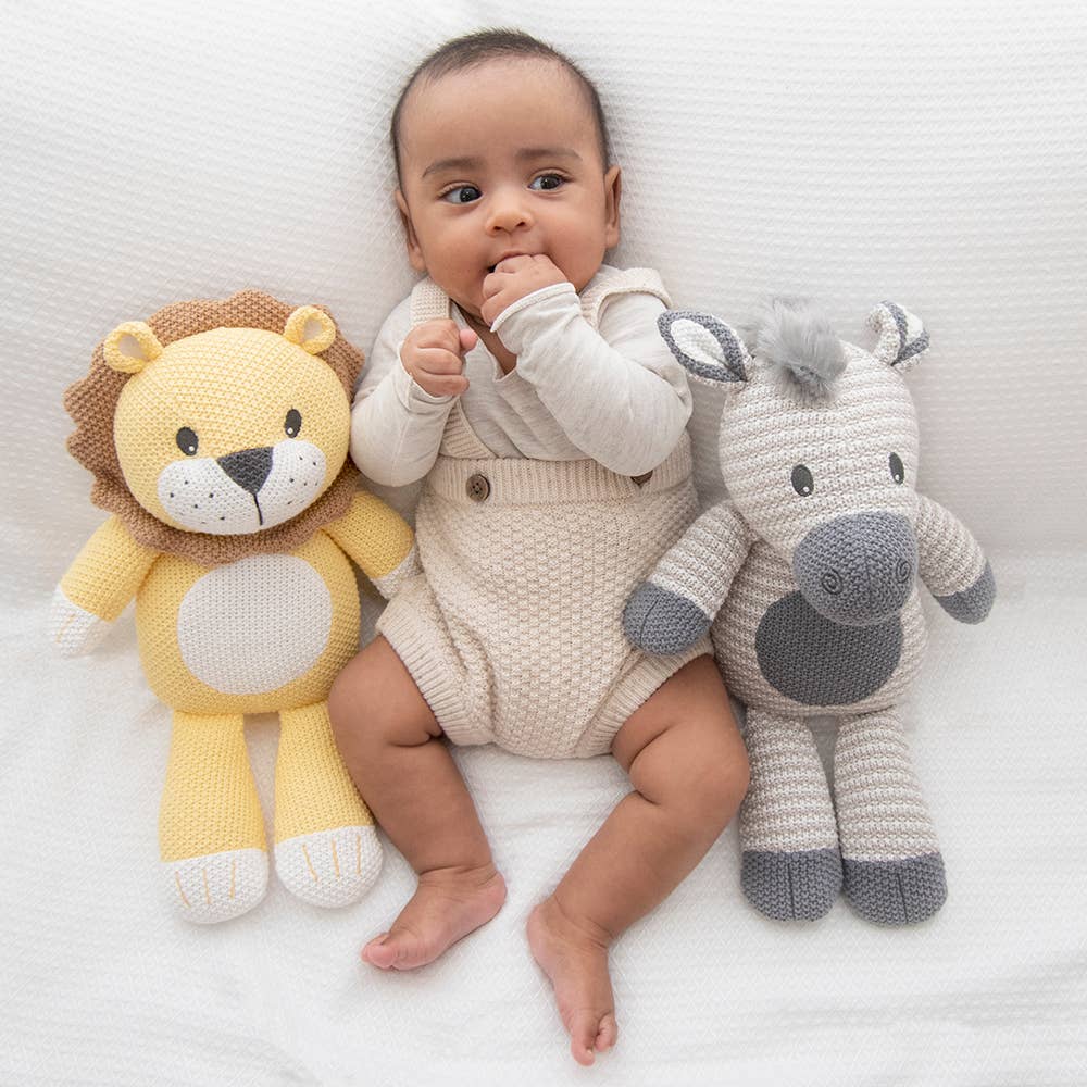 Baby lying between a lion and a horse stuffed toy on a white blanket