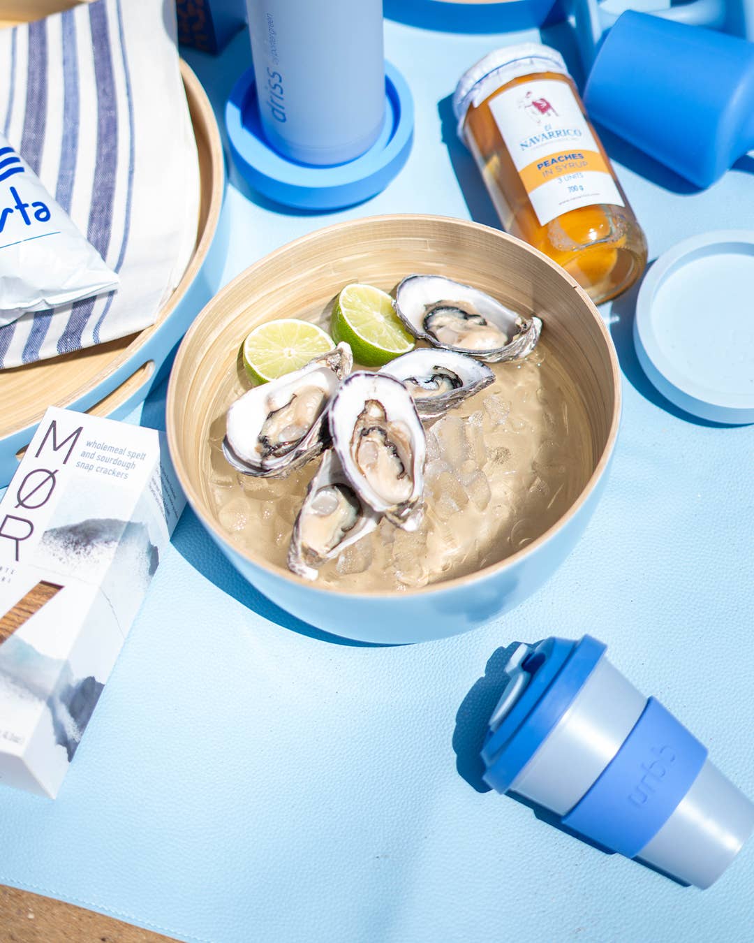 Bowl of oysters with lime wedges on a blue surface with various items around