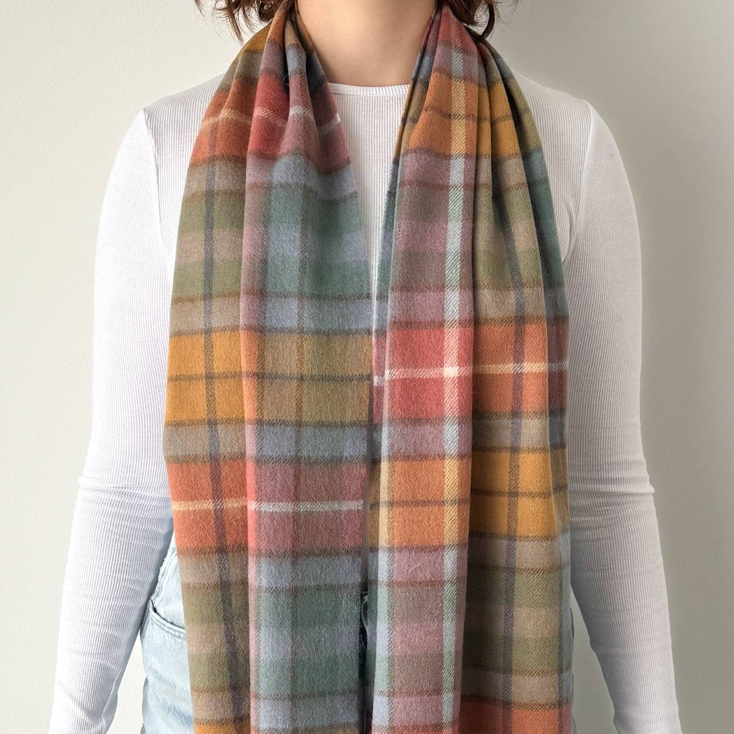 Person wearing a plaid scarf with autumn colors on a plain background