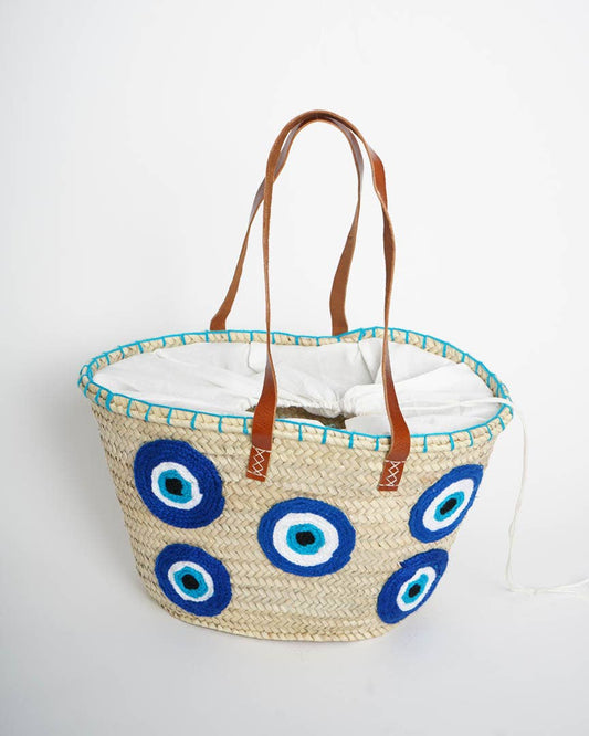 Woven basket with blue eye designs and brown handles on a white background