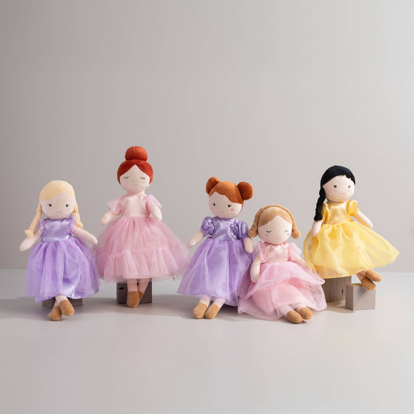 Five dolls in colorful dresses arranged in a row on a light gray background