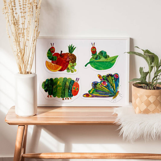 Framed artwork of caterpillars and fruits on a wooden table with plants and decor.