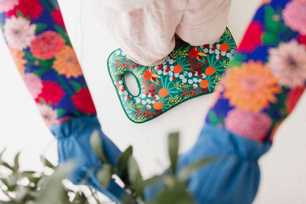 Person wearing colorful gloves with floral patterns holding a green mask with floral design.