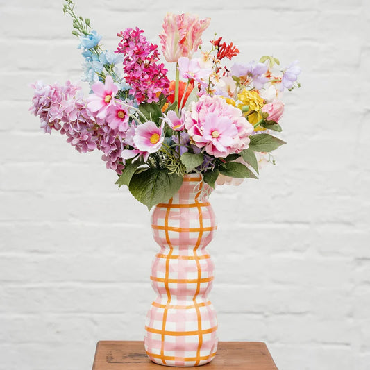 Decorative vase with a plaid pattern holding a bouquet of colorful flowers on a wooden surface.