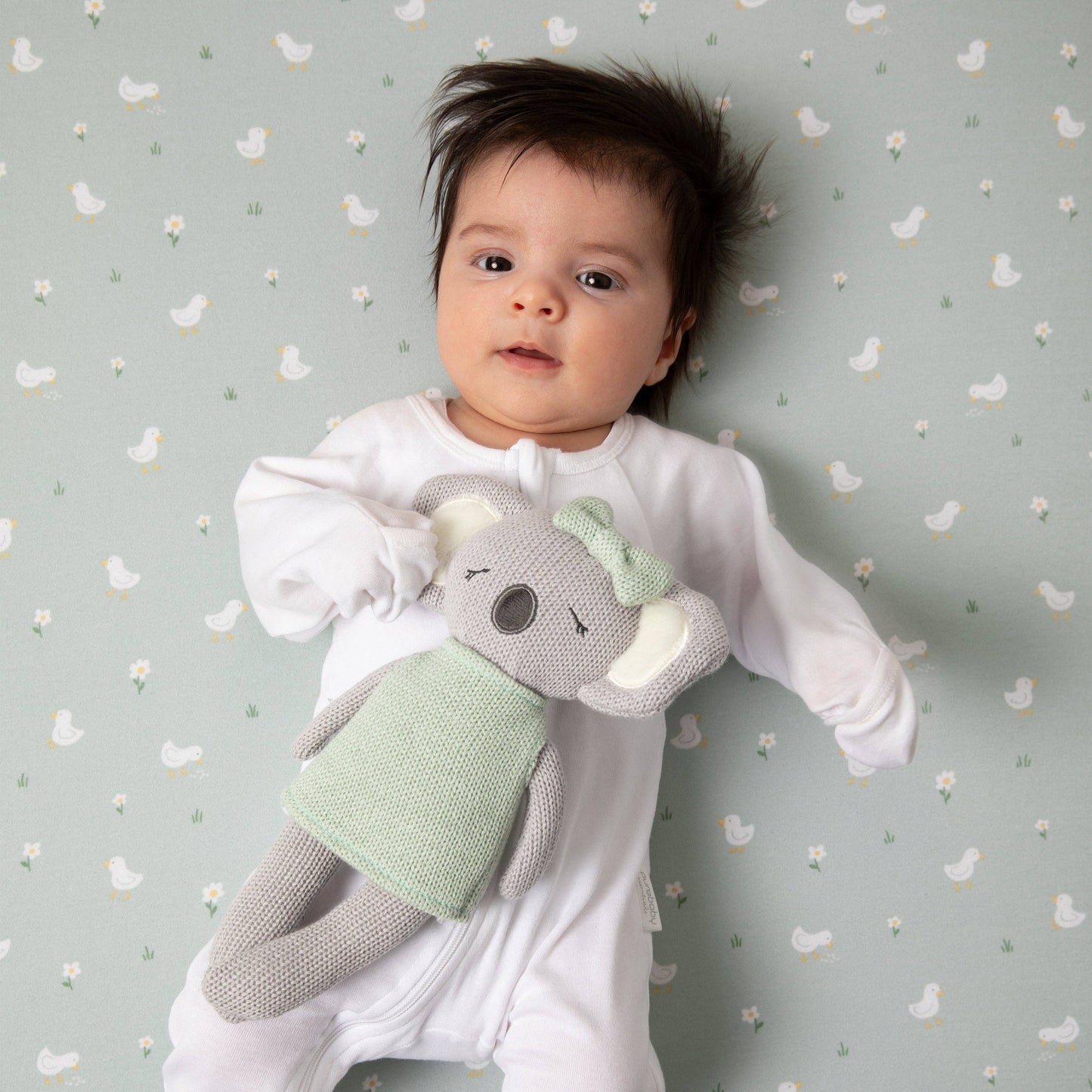 Baby holding a knitted elephant toy against a patterned background