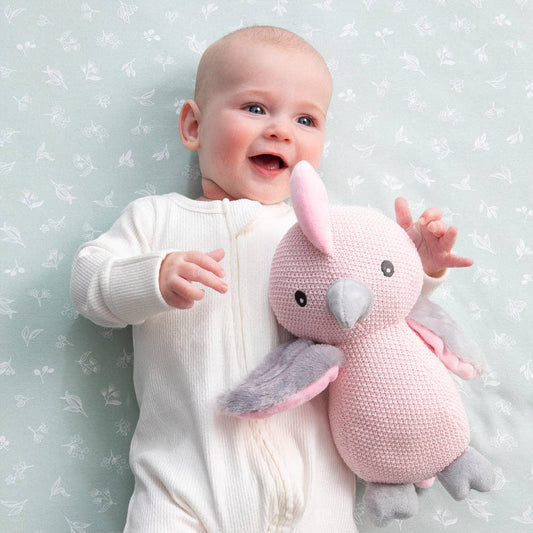 Baby holding a pink and gray stuffed animal against a light blue background