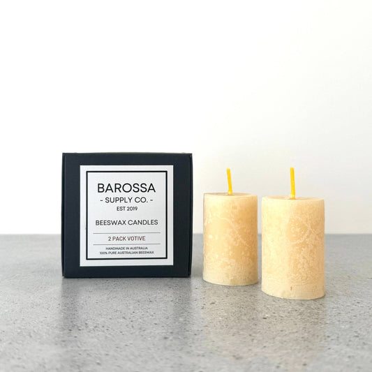 Two beeswax candles with a Barossa Supply Co. packaging box on a light surface.