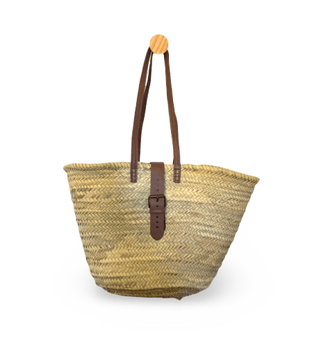 A natural straw tote bag with dark brown leather handles and a matching front strap, displayed on a white circular pedestal against a solid green background.