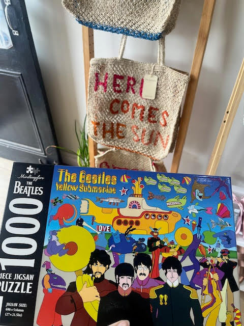 Jigsaw puzzle box featuring The Beatles and a woven bag with 'Here Comes the Sun' text.