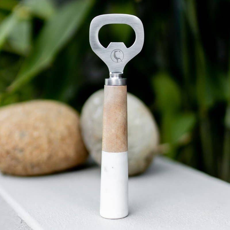 Bottle opener with cork and white design on a surface with blurred greenery in the background