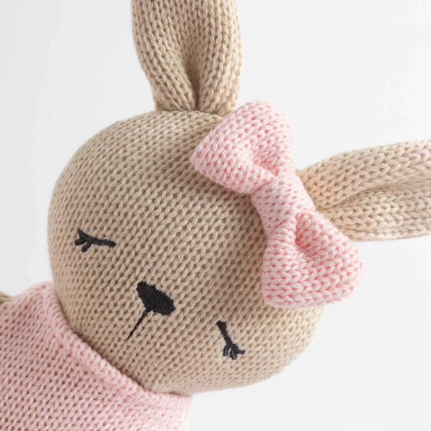 Knitted bunny toy with a pink bow on a white background