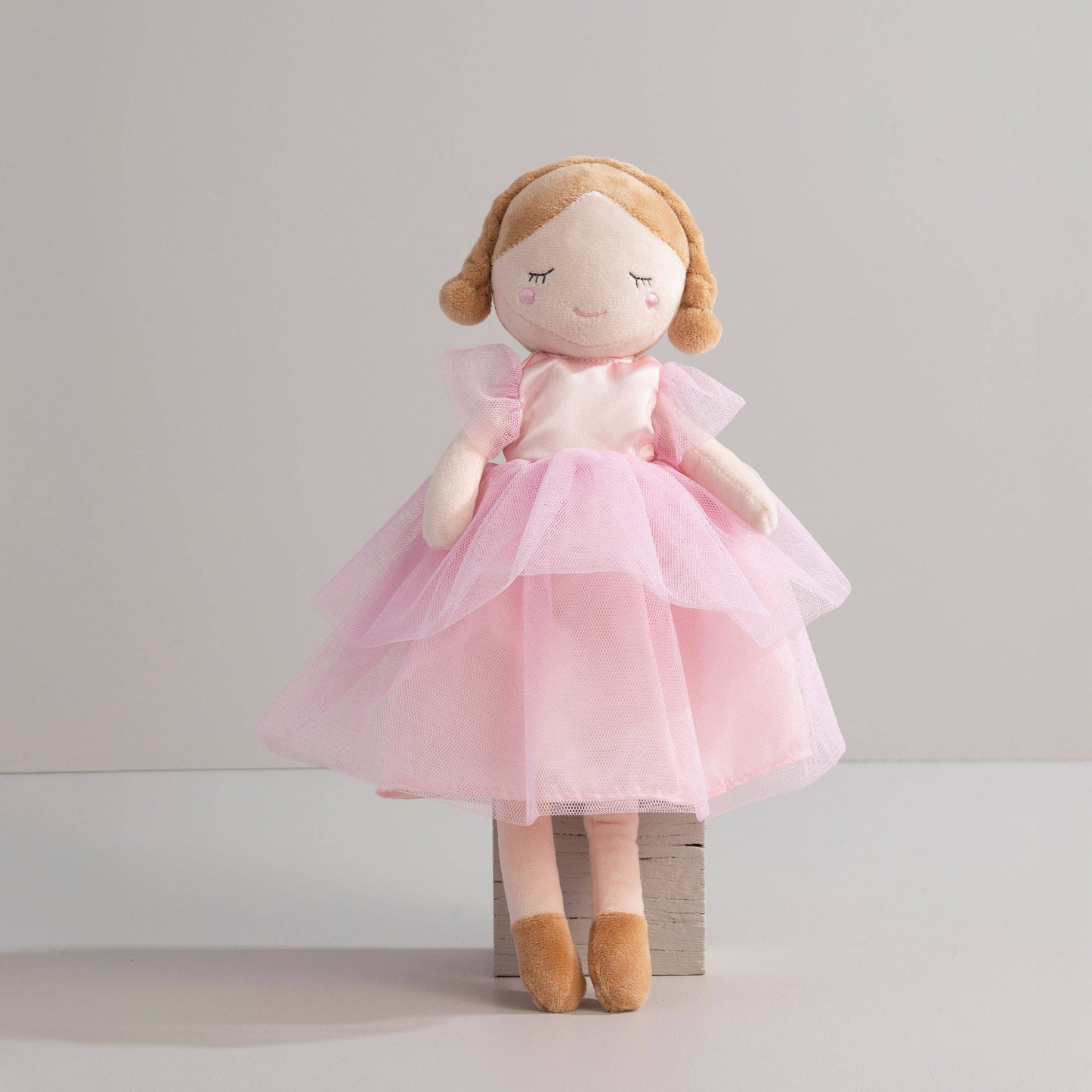Stuffed doll with a pink dress and brown hair on a light gray background
