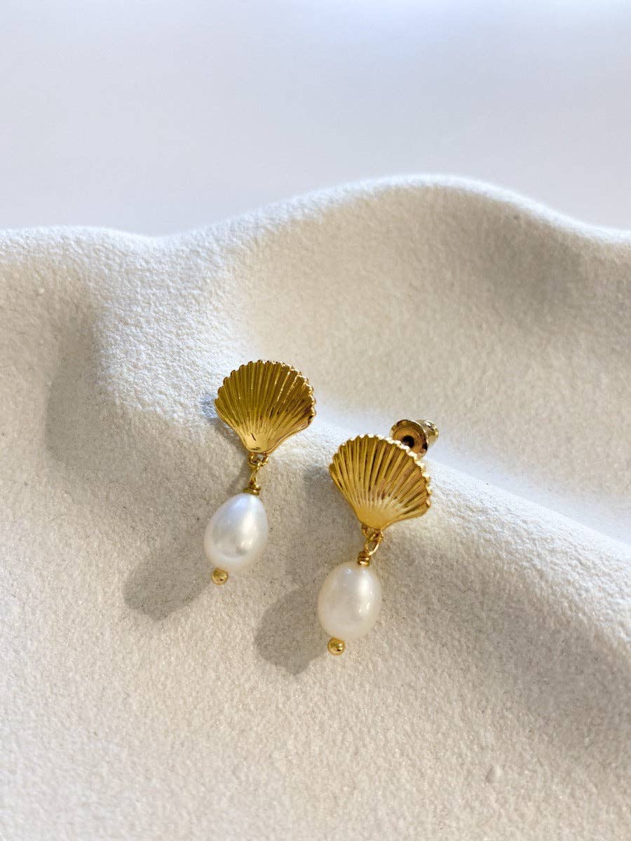 Gold shell-shaped earrings with pearl drops on a white fabric background