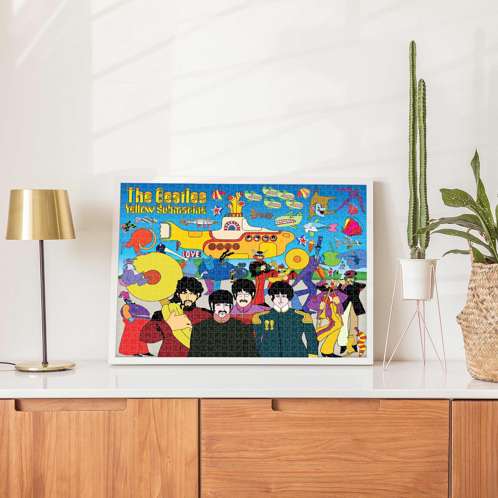 Framed poster of The Beatles' 'Yellow Submarine' on a white wall above a wooden cabinet.