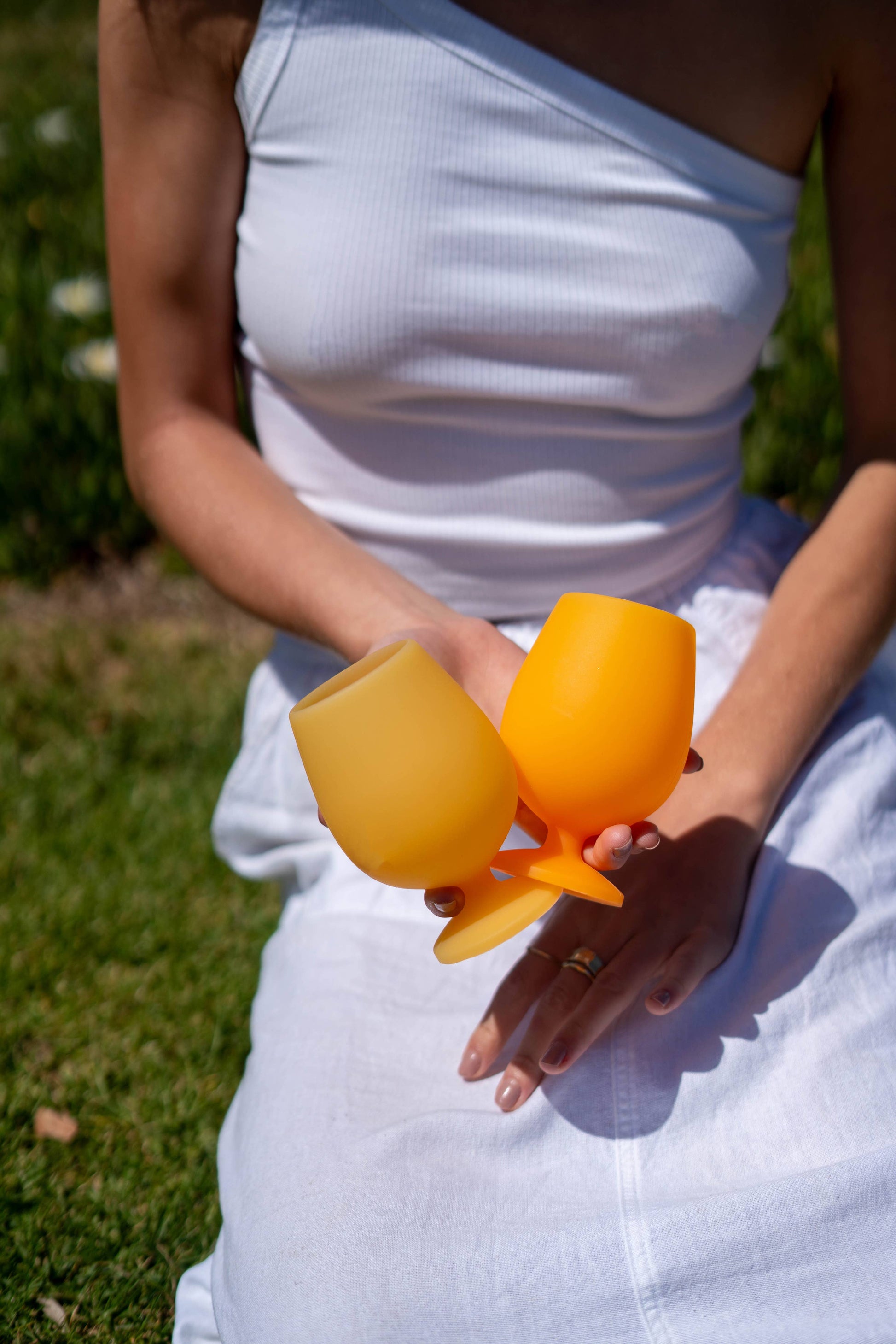 Person holding two yellow silicone cups outdoors on a grassy background