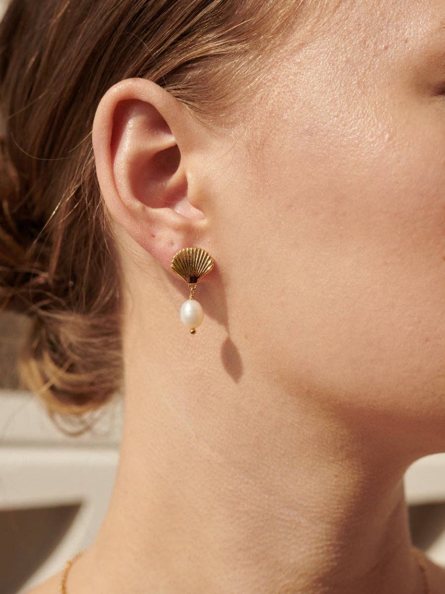 Close-up of a person wearing a gold earring with a pearl drop.