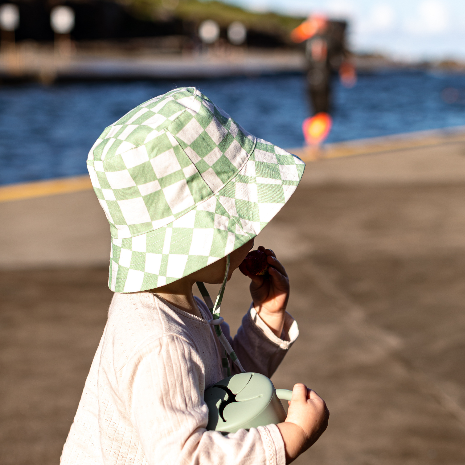 Child wearing a green checkered hat by a waterfront
