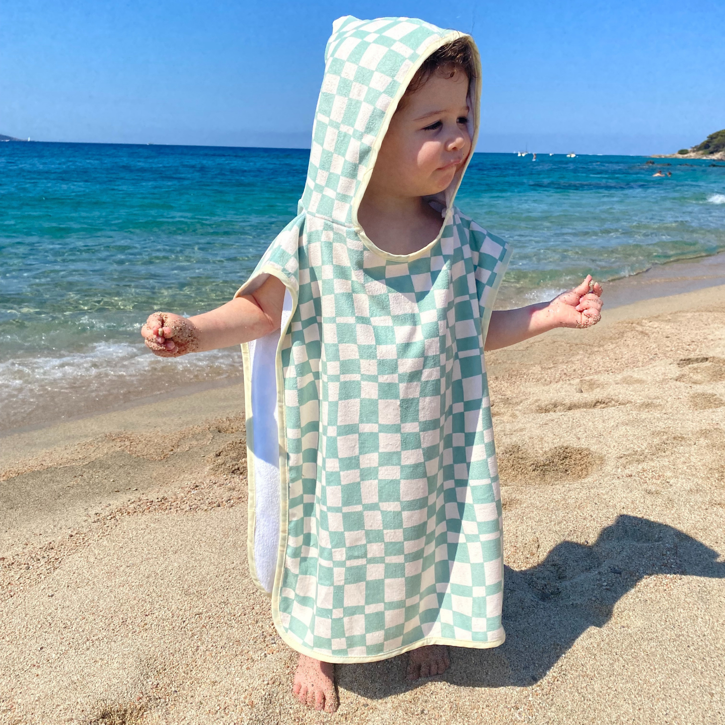 Child wearing a checkered hooded towel on a beach