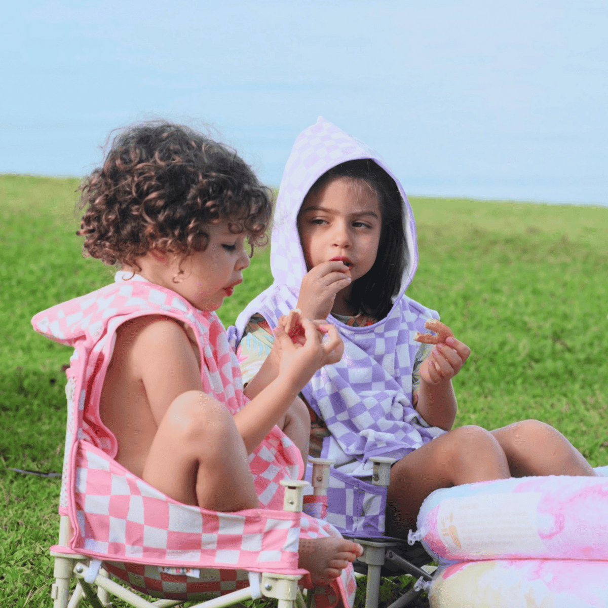 Two children sitting on a grassy field wearing checkered ponchos.