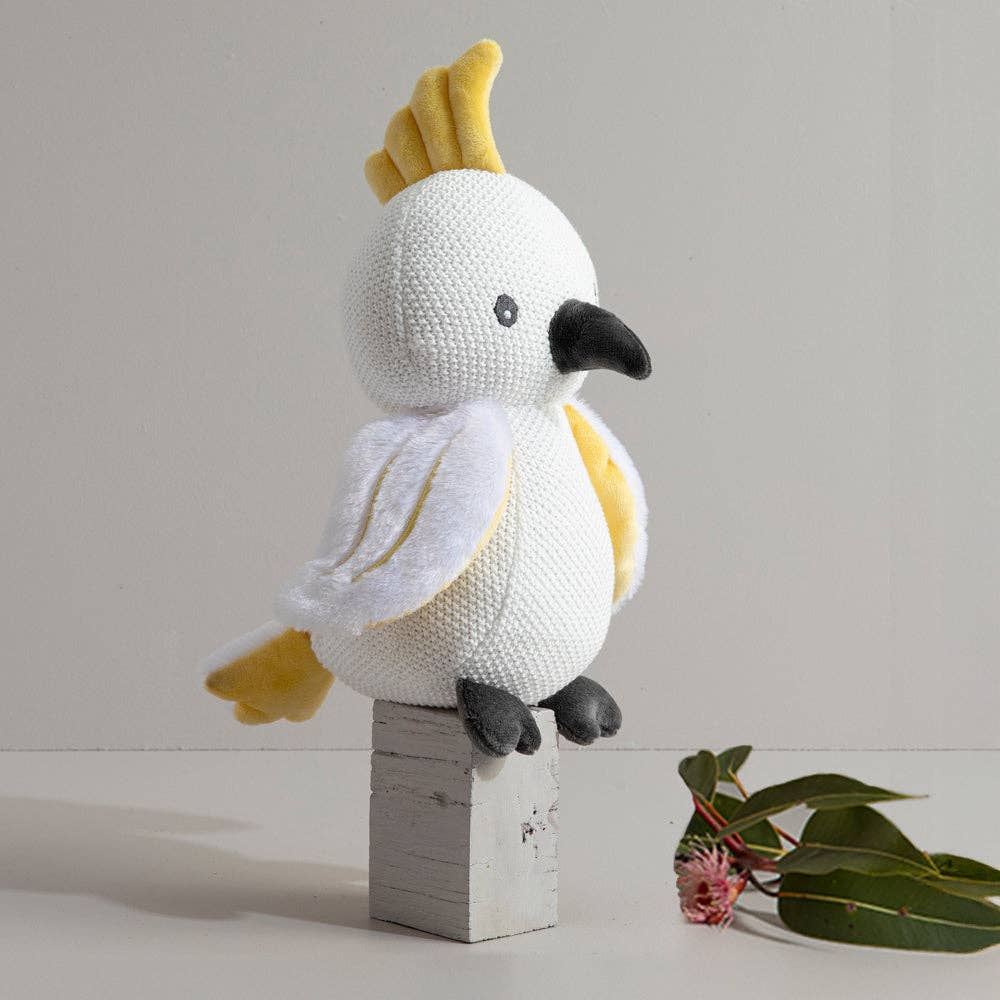 Knitted toy bird with yellow crest on a wooden block against a light background