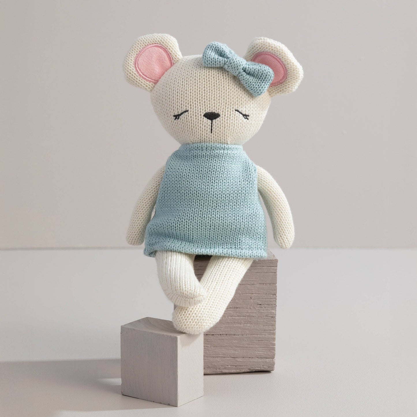 Knitted toy mouse in a blue dress with a bow on a light background