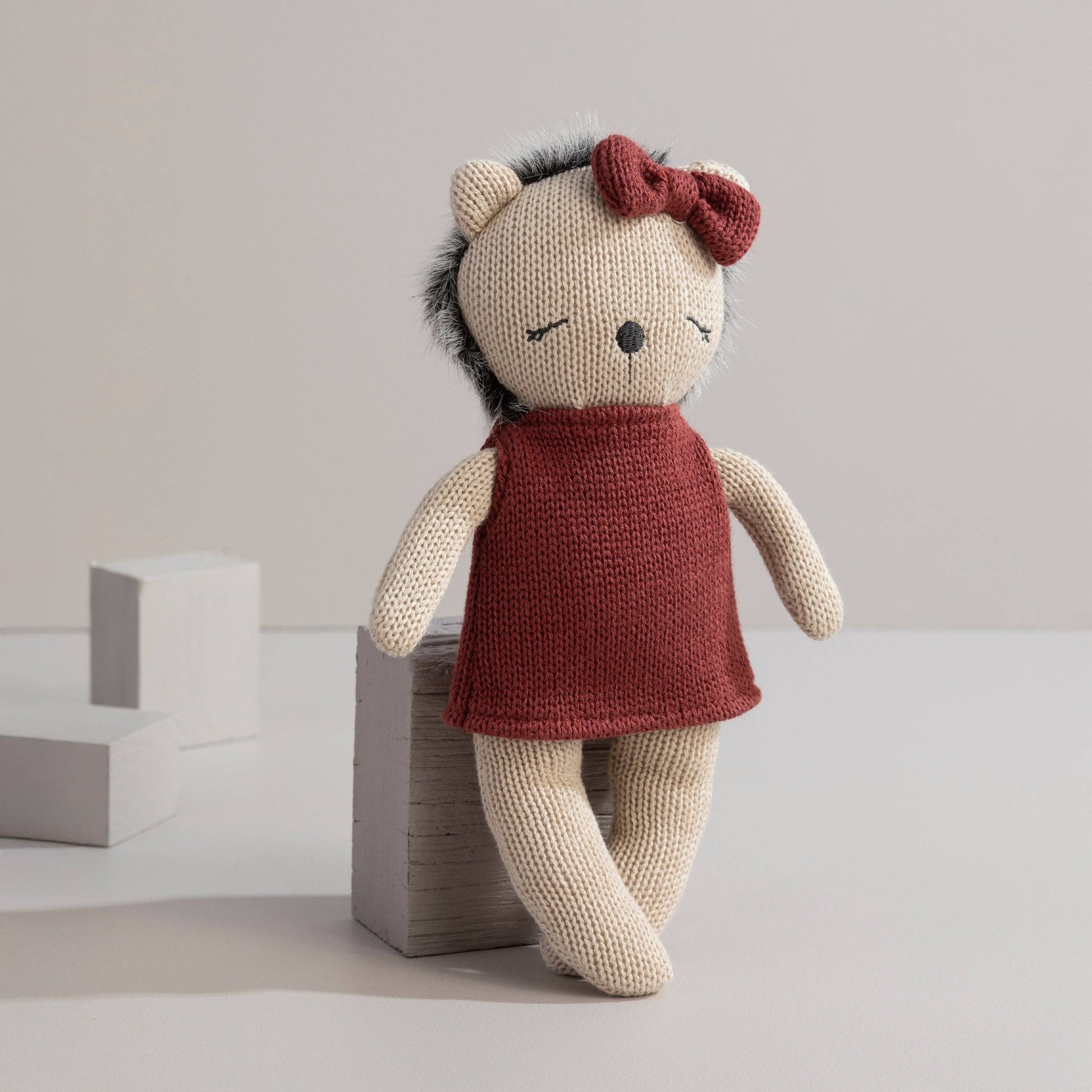 Knitted toy wearing a red dress and bow on a neutral background