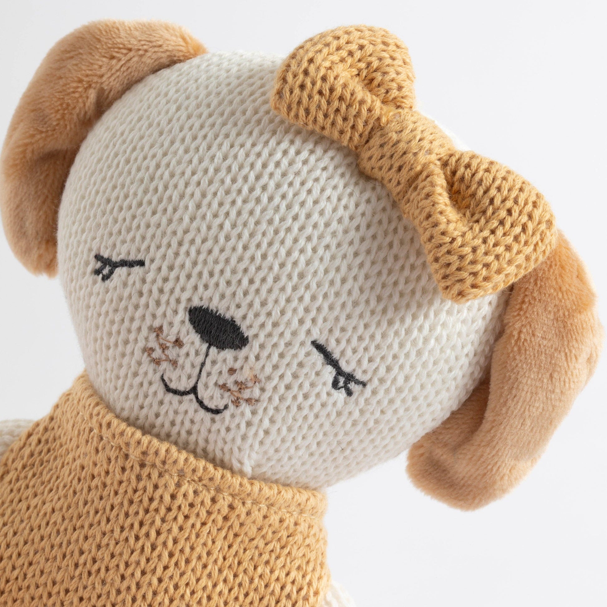 Knitted dog toy with a white face and brown ears on a light background