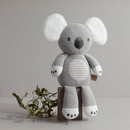 Knitted koala toy on a wooden block with a plain background