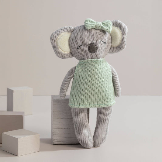 Knitted toy mouse in a green dress with a bow on a neutral background
