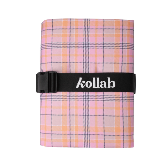 A folded plaid fabric item, likely a scarf or pocket square, in pink, orange, and white with a black elastic band across the middle featuring the white 'kollab' logo.
