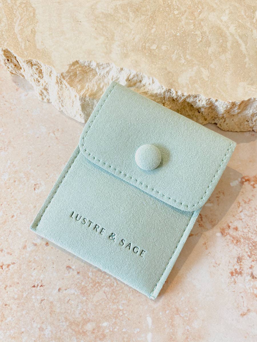 sage jewelry pouch with 'Lustre & Sage' branding on a beige stone surface