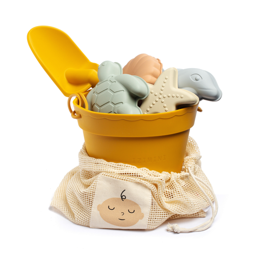 Yellow bucket with bath toys including a turtle, starfish, and fish, accompanied by a mesh bag with a baby design.