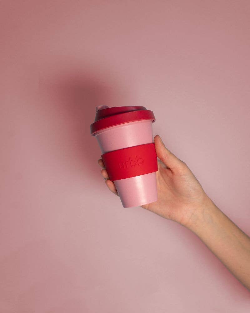 Hand holding a red reusable coffee cup against a pink background