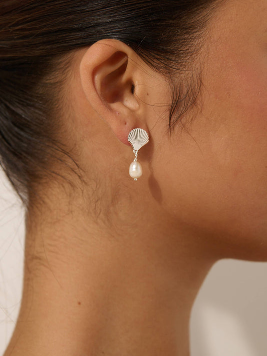 A person wearing a pearl earring with a silver clasp, showcasing a clamshell design.