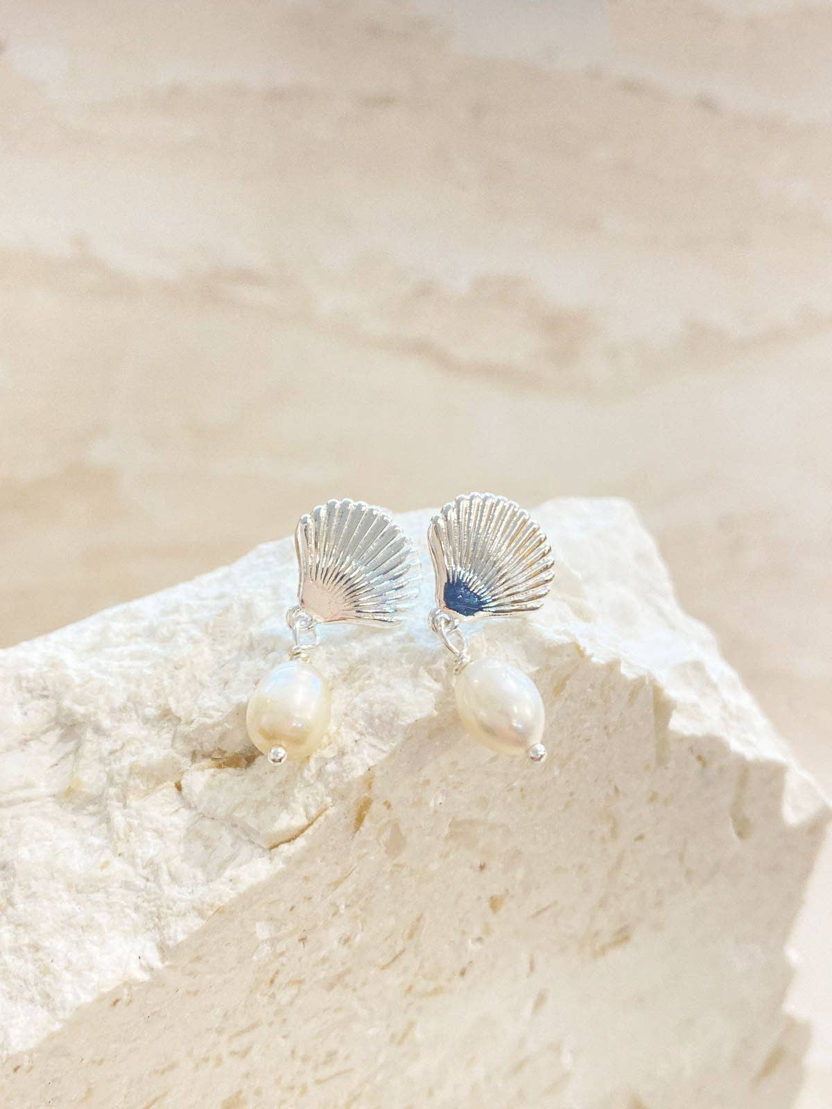 Silver shell earrings on a white shell with a beige sand background