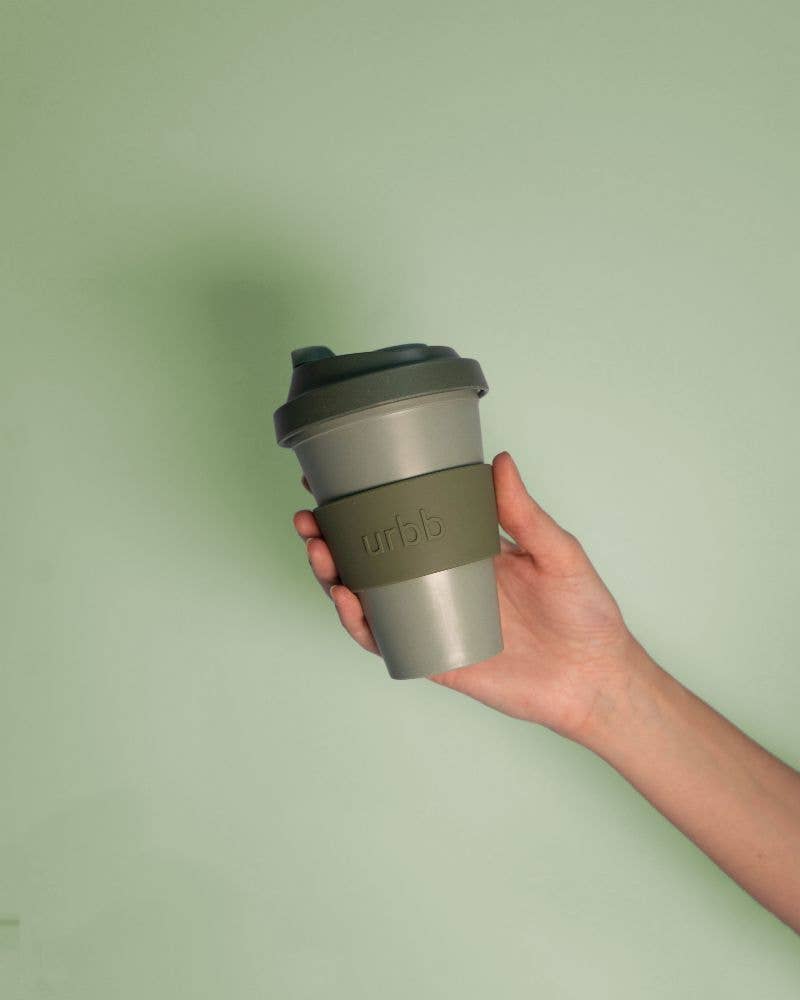 Hand holding a reusable coffee cup with a green lid against a light green background