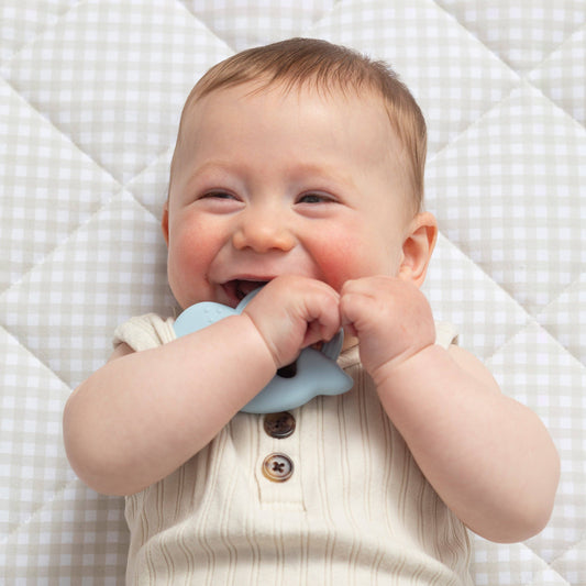 Baby lying on a checkered blanket with a blue teething ring