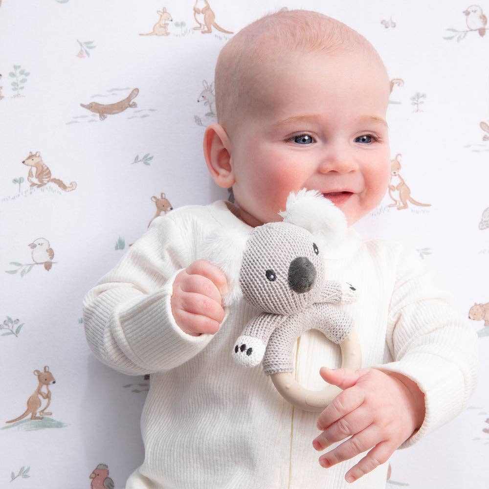 Baby holding a koala toy against a patterned background
