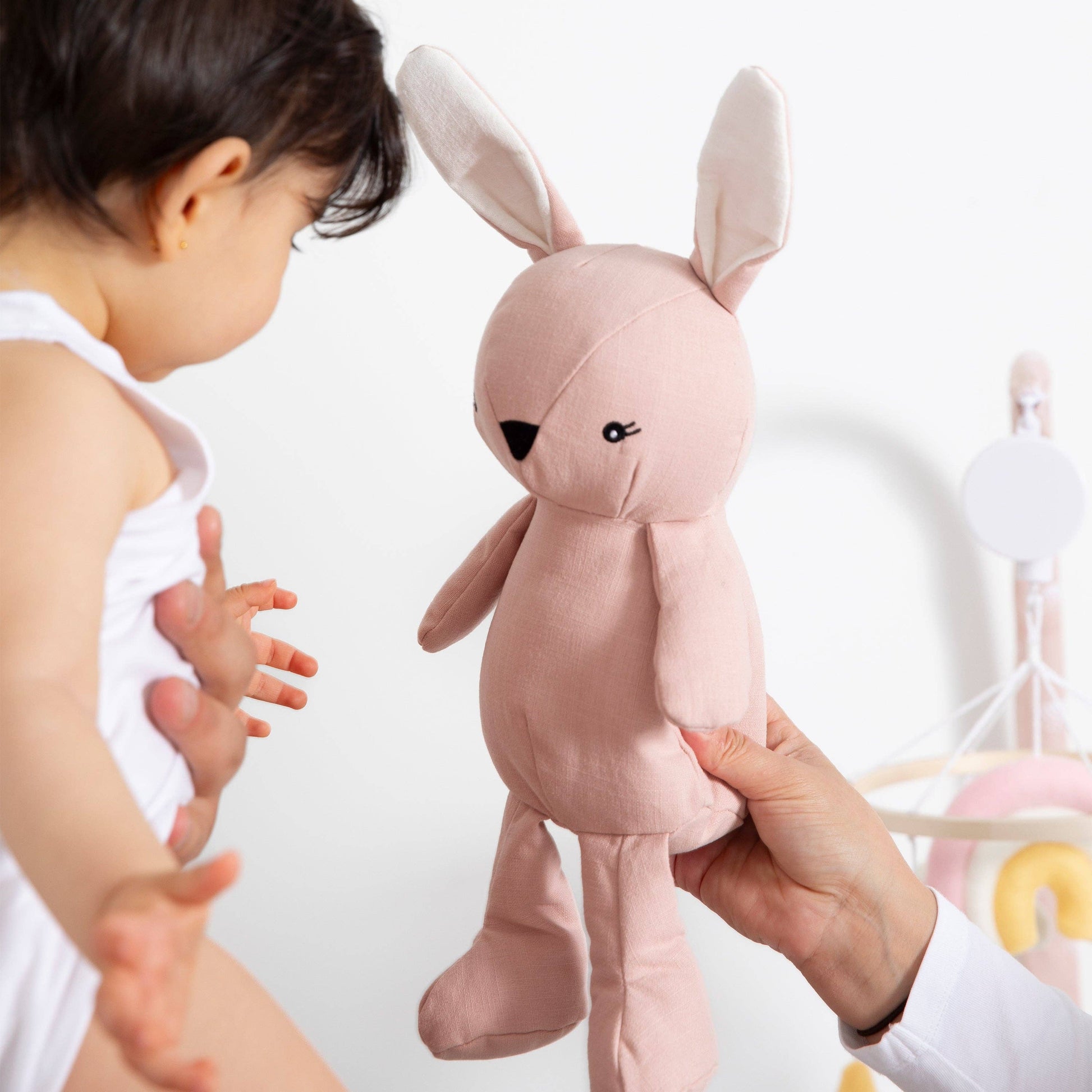 Baby interacting with a pink plush toy resembling a rabbit.