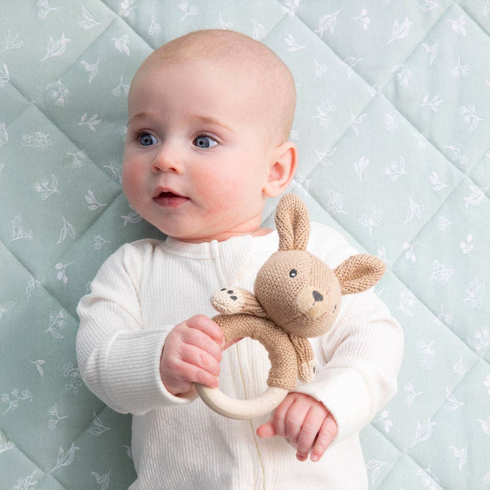 Baby holding a Kangaroo rattle  against a light blue quilted background