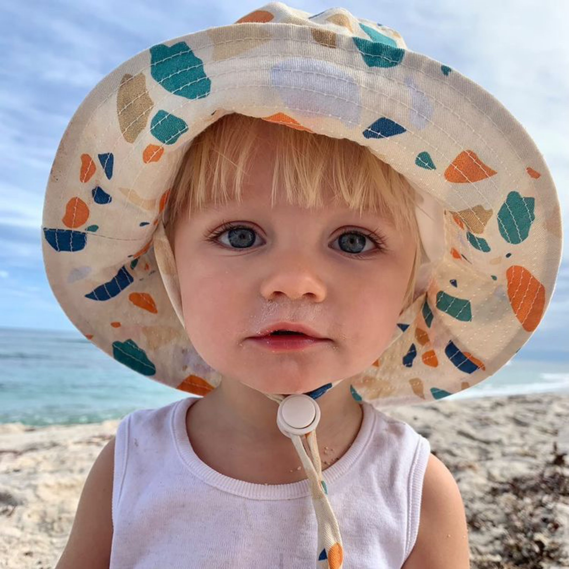 Child wearing a colorful sun hat on a beach