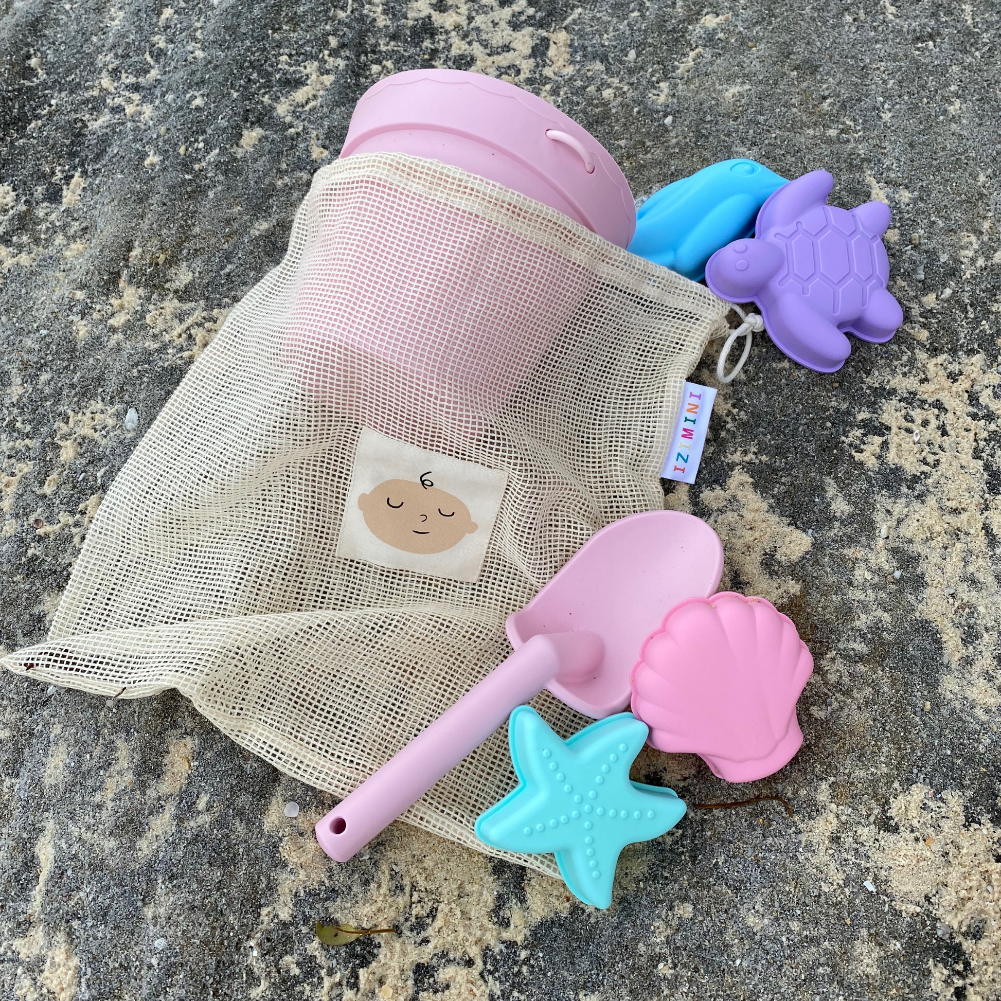 Set of beach toys including a pink bucket, spade, and molds on a stone surface.
