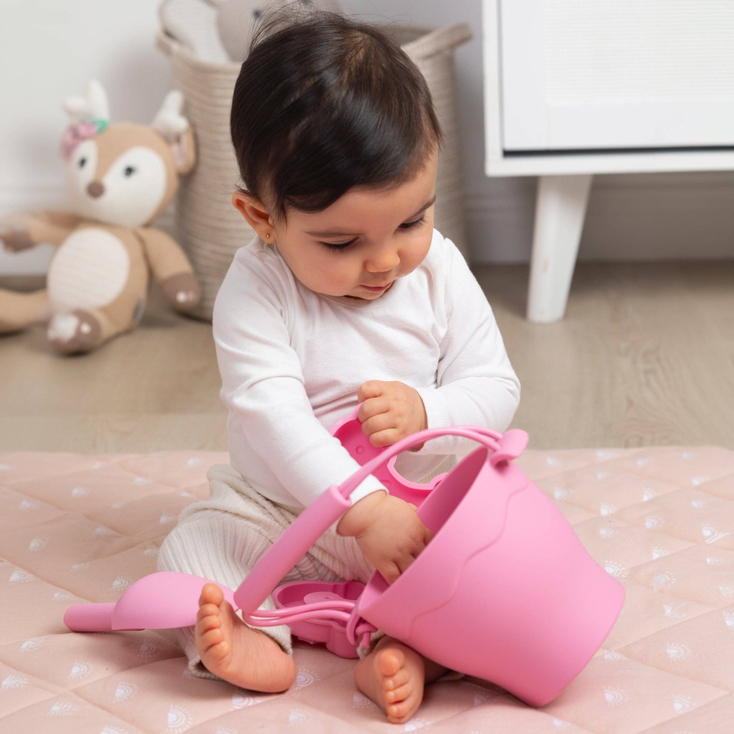 Child playing with a pink sand pail and shovel on a bed