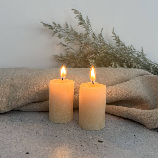 Two lit candles on a textured surface with a neutral background