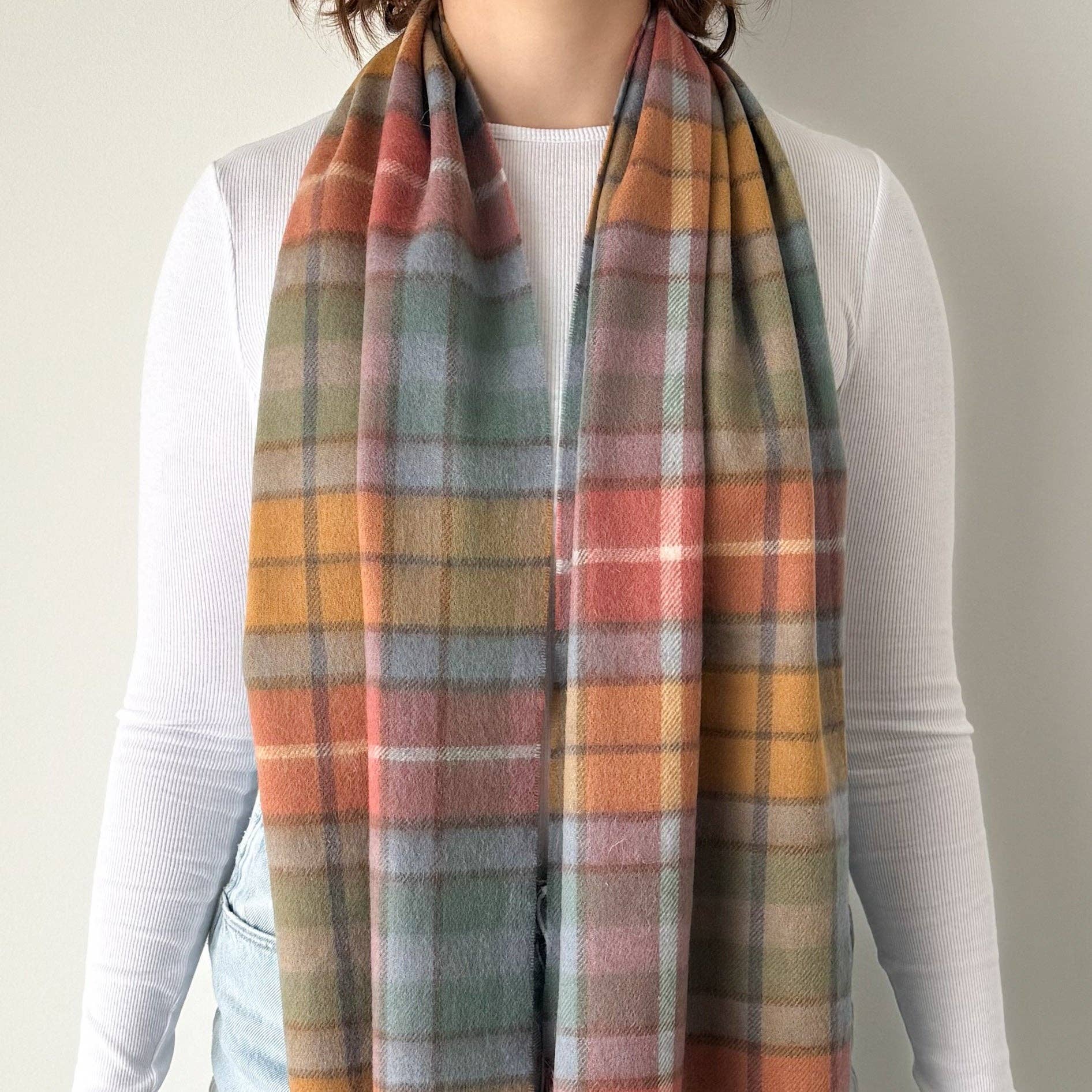 Person wearing a plaid scarf with autumn colors on a plain background